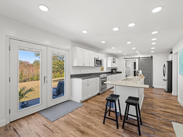 kitchen with stainless steel appliances, hardwood / wood-style flooring, a barn door, sink, and white cabinetry