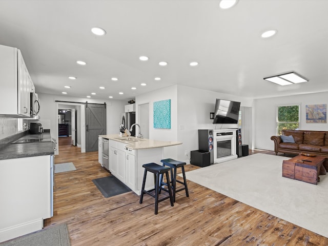 kitchen featuring white cabinetry, a center island with sink, appliances with stainless steel finishes, a barn door, and light wood-type flooring