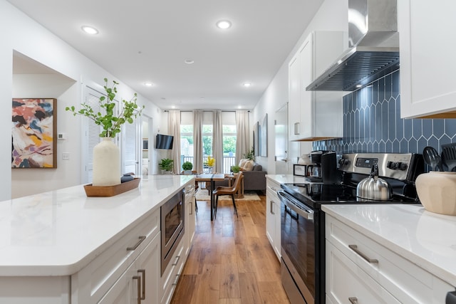 kitchen featuring stainless steel appliances, white cabinetry, wall chimney exhaust hood, light wood-type flooring, and decorative backsplash