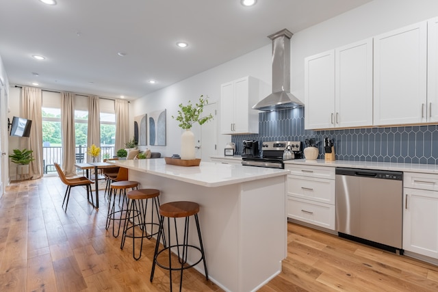 kitchen with wall chimney exhaust hood, white cabinetry, a kitchen island, and appliances with stainless steel finishes