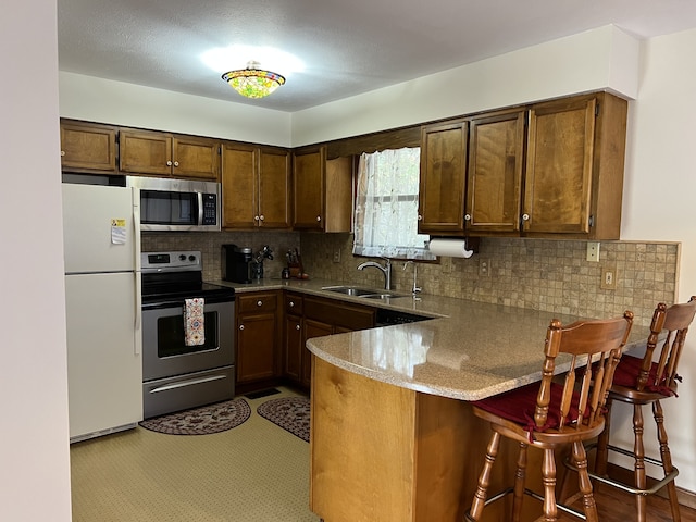 kitchen with a kitchen bar, kitchen peninsula, sink, tasteful backsplash, and appliances with stainless steel finishes