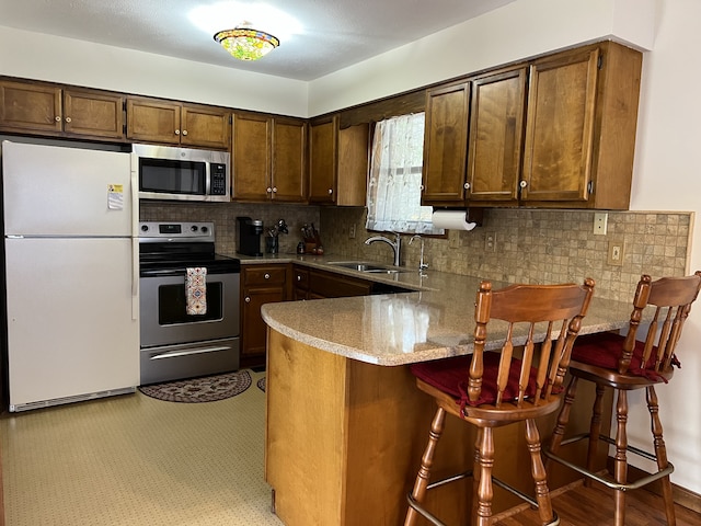 kitchen featuring stainless steel appliances, sink, a breakfast bar, kitchen peninsula, and tasteful backsplash