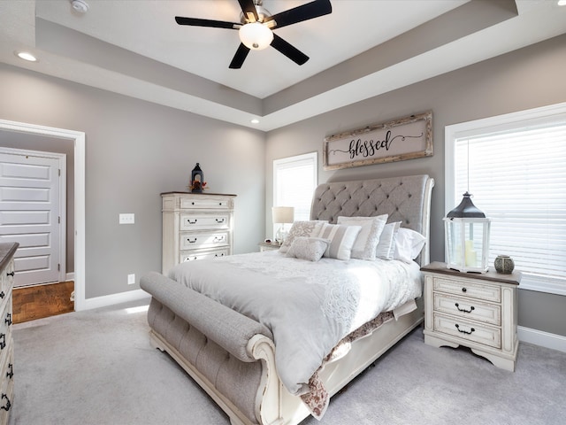 carpeted bedroom with ceiling fan and a raised ceiling