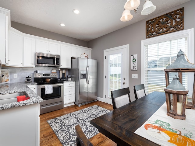 kitchen with stainless steel appliances, light stone counters, tasteful backsplash, wood-type flooring, and white cabinets