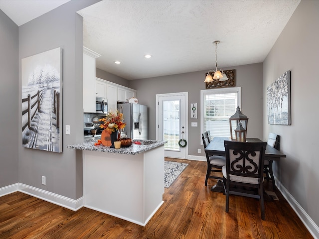 kitchen with white cabinetry, appliances with stainless steel finishes, decorative light fixtures, and dark hardwood / wood-style flooring