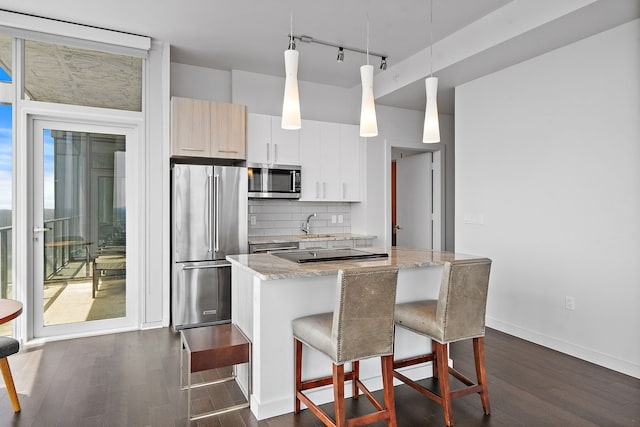 kitchen with light stone counters, stainless steel appliances, a kitchen island, white cabinetry, and hanging light fixtures