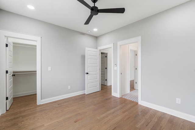 unfurnished bedroom featuring a closet, light wood-type flooring, a spacious closet, and ceiling fan