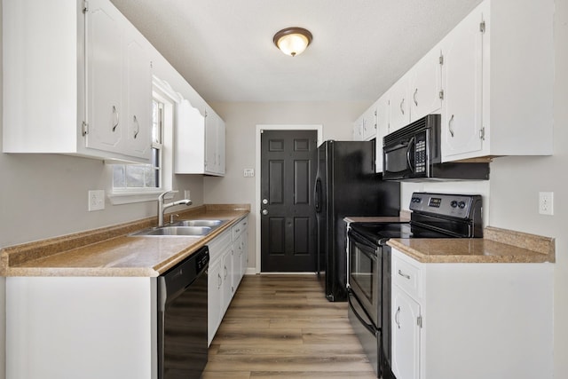 kitchen with sink, a textured ceiling, white cabinets, black appliances, and hardwood / wood-style flooring