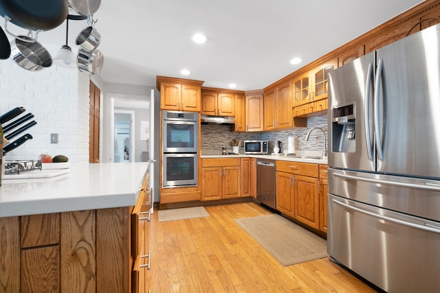 kitchen with light wood-type flooring, appliances with stainless steel finishes, sink, and backsplash