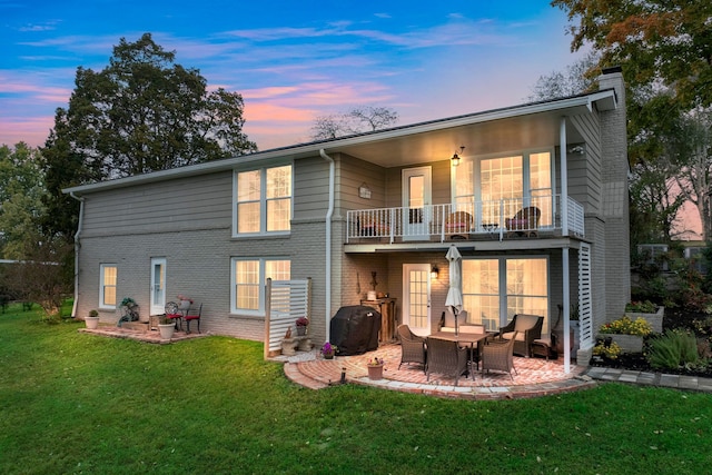 back house at dusk featuring a patio, a lawn, and a balcony