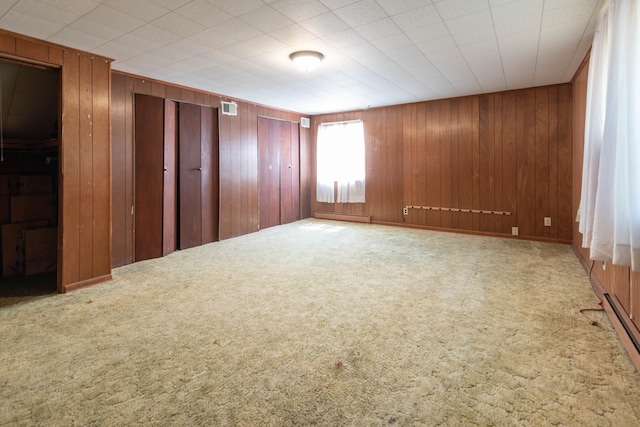 carpeted spare room with baseboard heating and wood walls