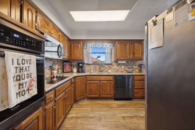 kitchen with light stone counters, black appliances, sink, backsplash, and light hardwood / wood-style flooring