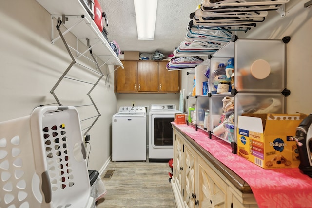 laundry room with a textured ceiling, separate washer and dryer, light hardwood / wood-style floors, and cabinets