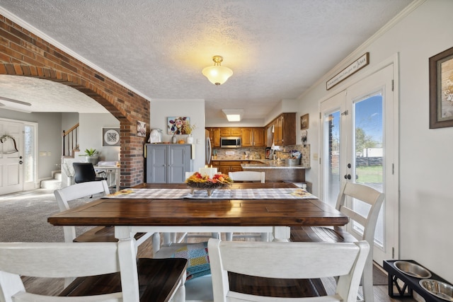 carpeted dining area with brick wall, a textured ceiling, and crown molding