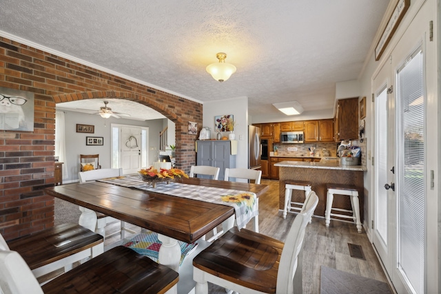 dining space featuring a textured ceiling, brick wall, hardwood / wood-style flooring, and ceiling fan