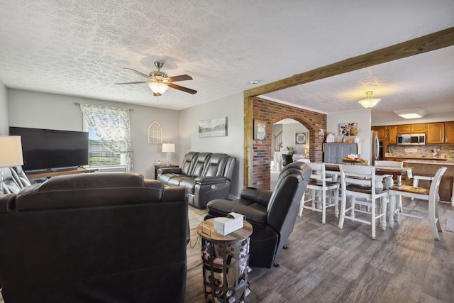 living room featuring hardwood / wood-style floors, ceiling fan, a textured ceiling, and brick wall