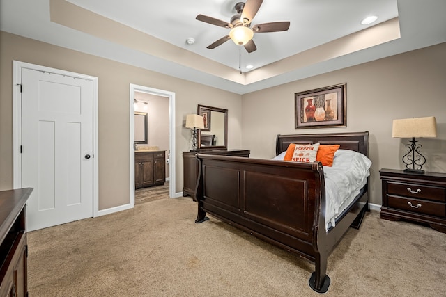 carpeted bedroom featuring ceiling fan, ensuite bath, and a raised ceiling