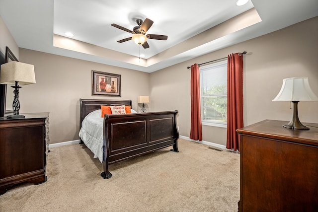 bedroom with ceiling fan, light carpet, and a raised ceiling