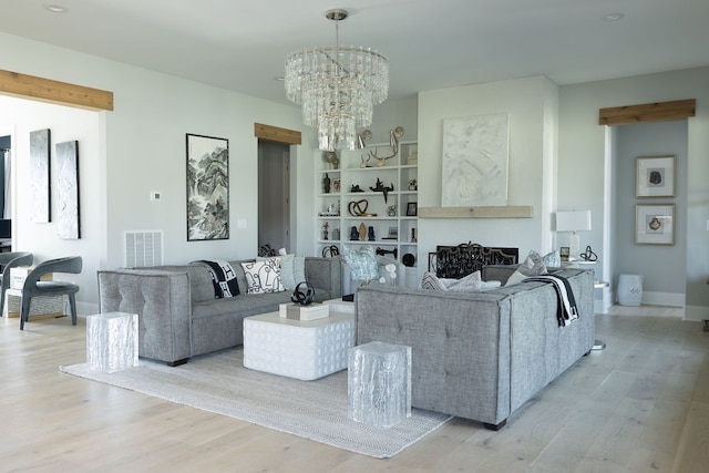 living area featuring built in features, visible vents, light wood-style flooring, an inviting chandelier, and baseboards