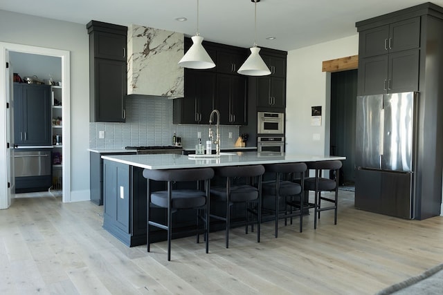 kitchen with pendant lighting, a center island with sink, stainless steel appliances, light countertops, and dark cabinets