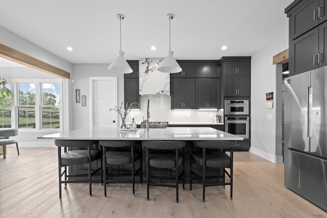 kitchen featuring a breakfast bar, hanging light fixtures, appliances with stainless steel finishes, a kitchen island with sink, and dark cabinets