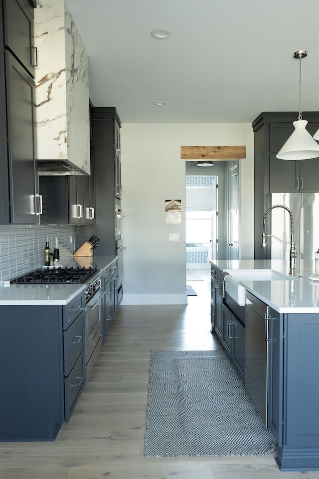 kitchen featuring tasteful backsplash, light countertops, hanging light fixtures, a sink, and light wood-type flooring