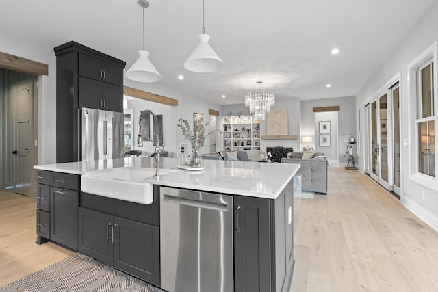 kitchen featuring a center island with sink, stainless steel appliances, light countertops, a sink, and dark cabinetry