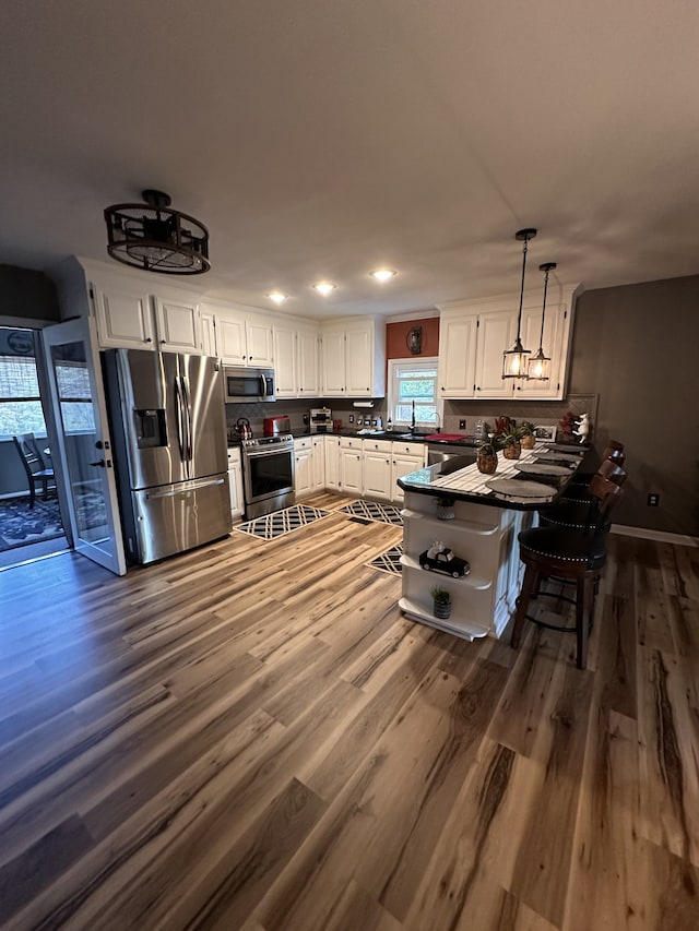 kitchen featuring white cabinetry, appliances with stainless steel finishes, dark hardwood / wood-style flooring, hanging light fixtures, and kitchen peninsula