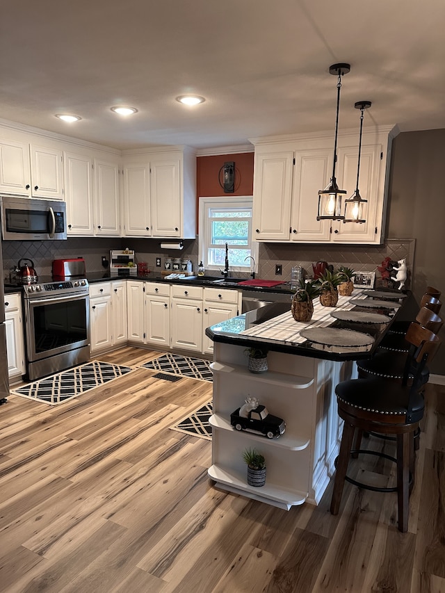 kitchen with white cabinets, kitchen peninsula, appliances with stainless steel finishes, and hanging light fixtures