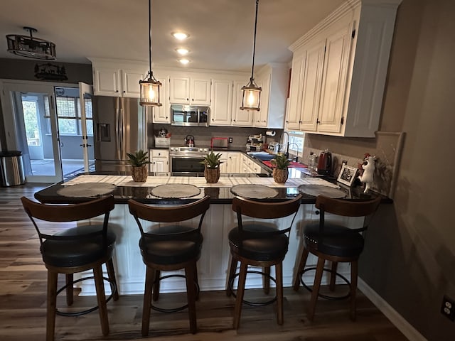 kitchen with stainless steel appliances, white cabinetry, dark hardwood / wood-style floors, pendant lighting, and sink