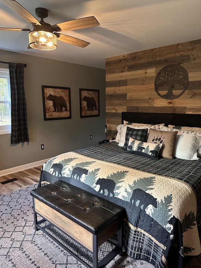 bedroom with wooden walls, hardwood / wood-style flooring, and ceiling fan