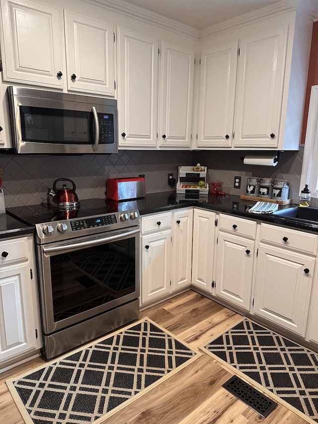 kitchen featuring tasteful backsplash, stainless steel appliances, white cabinetry, sink, and light hardwood / wood-style flooring