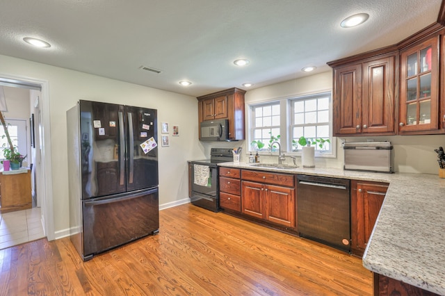 kitchen featuring black appliances, light stone counters, a textured ceiling, sink, and light hardwood / wood-style flooring