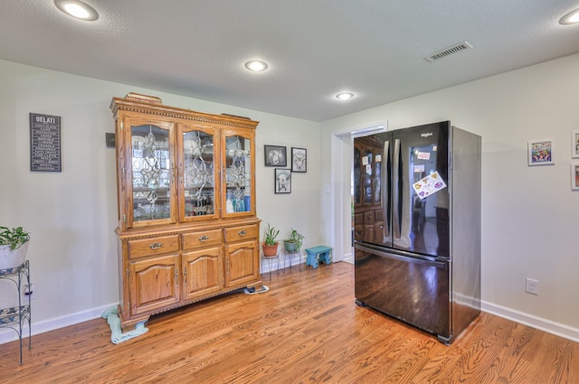 kitchen with light hardwood / wood-style floors, a textured ceiling, and black refrigerator