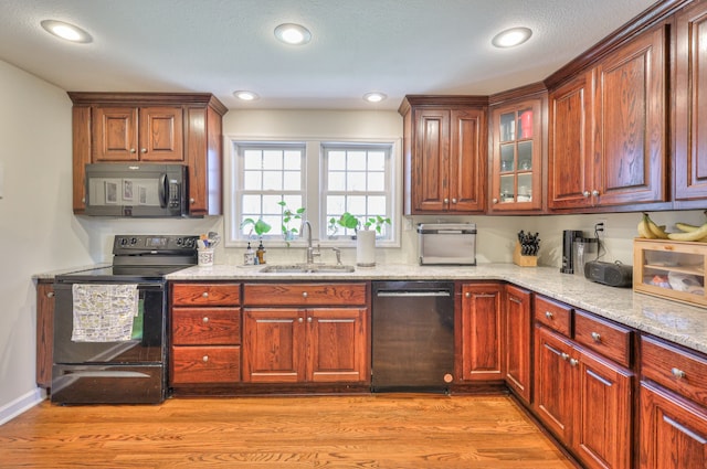 kitchen with light hardwood / wood-style floors, light stone counters, black appliances, a textured ceiling, and sink