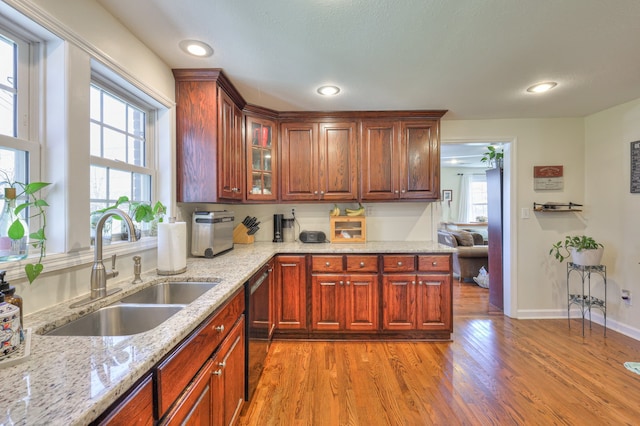 kitchen with light hardwood / wood-style floors, sink, light stone counters, and black dishwasher