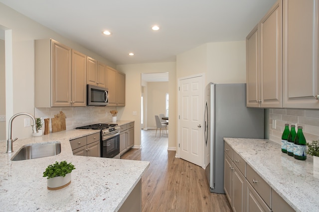 kitchen with light hardwood / wood-style floors, stainless steel appliances, sink, backsplash, and light stone countertops