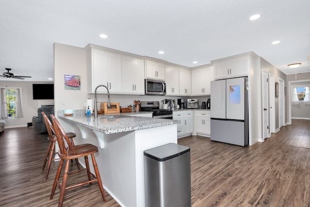 kitchen featuring kitchen peninsula, sink, light stone countertops, white cabinetry, and appliances with stainless steel finishes