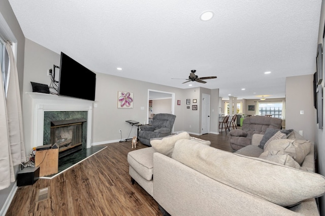 living room featuring a textured ceiling, dark wood-type flooring, ceiling fan, and a high end fireplace