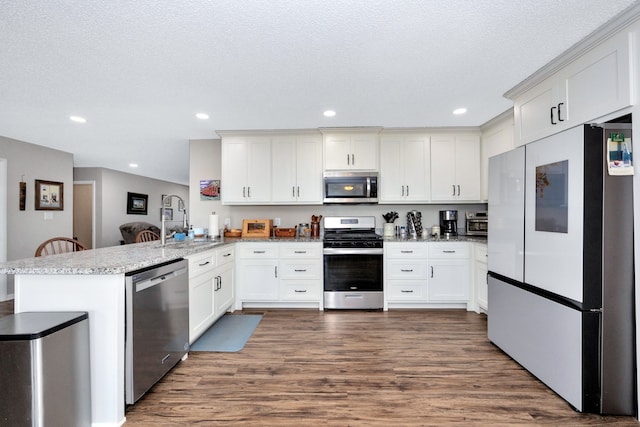 kitchen featuring dark hardwood / wood-style flooring, kitchen peninsula, sink, white cabinetry, and appliances with stainless steel finishes