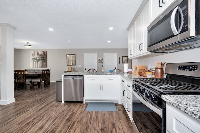 kitchen with white cabinetry, appliances with stainless steel finishes, dark hardwood / wood-style flooring, light stone countertops, and kitchen peninsula