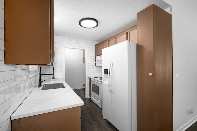 kitchen with dark wood-type flooring, white appliances, sink, and a textured ceiling