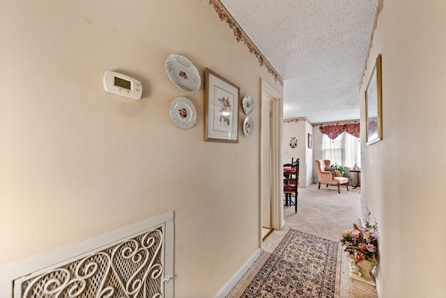 corridor with a textured ceiling and light colored carpet