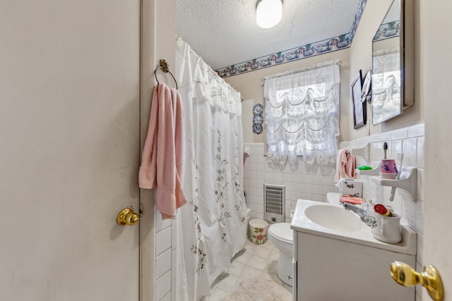 full bathroom featuring a textured ceiling, vanity, tile patterned floors, toilet, and tile walls