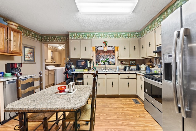 kitchen with light hardwood / wood-style floors, stainless steel appliances, a textured ceiling, sink, and washer / dryer