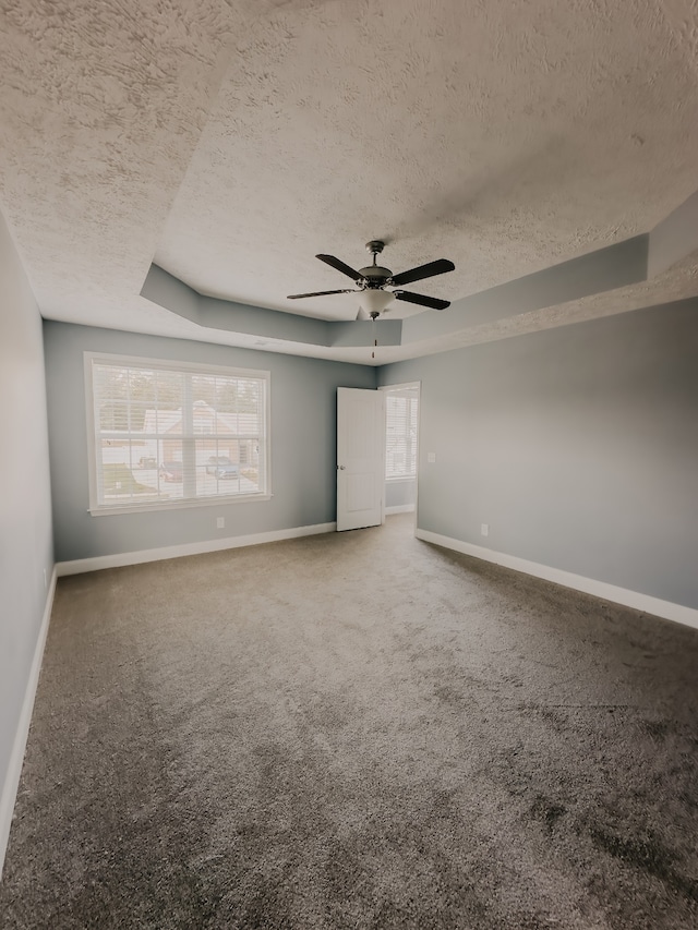 carpeted empty room featuring a textured ceiling, ceiling fan, and a tray ceiling