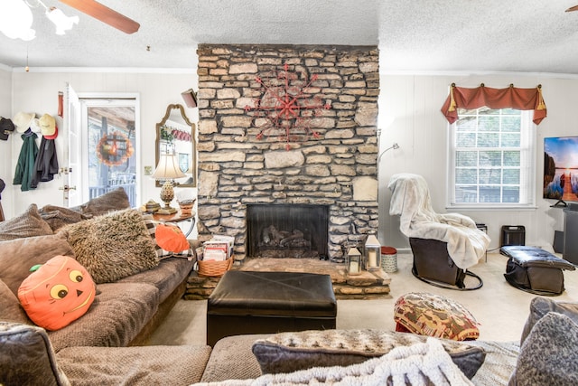 carpeted living room with ceiling fan, a fireplace, a textured ceiling, and ornamental molding