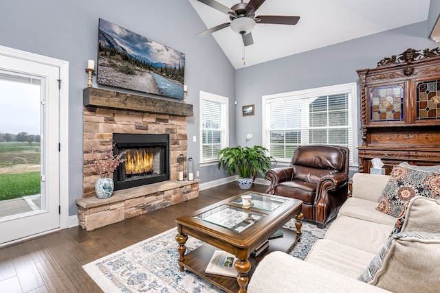 living room featuring a stone fireplace, high vaulted ceiling, dark wood-type flooring, and ceiling fan