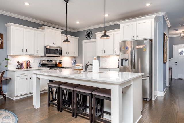 kitchen featuring appliances with stainless steel finishes, decorative light fixtures, an island with sink, white cabinets, and dark wood-type flooring