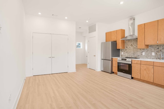 kitchen with appliances with stainless steel finishes, light hardwood / wood-style floors, wall chimney range hood, and backsplash